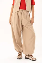 Pantalon tipo babucha de color beige, con silueta relajada y acabado suave tipo piel de durazno. Presenta cintura regulable con cordón y elástico en los tobillos que genera una forma abuchonada.