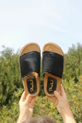 Sandalias de cuero negro con tira ancha de pelo y suela plana de corcho.
