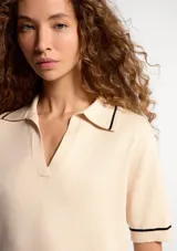 Polo de manga corta en tejido de punto color beige, con cuello tipo polo y detalles de líneas finas en color negro en el cuello, mangas y ruedo.
