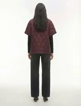 Poncho acolchado color vino tinto, con cuello alto y cierre frontal parcial. Presenta un patrón de costuras capitoné en forma de hoja o diamante y bolsillos delanteros.