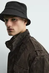 Cazadora de corte relajado confeccionada en piel con acabado de ante. Presenta cuello subido, cierre frontal de cremallera oculta por solapa con botones a presión, bolsillos de plastrón con solapa en el pecho y bolsillos de vivo en la cadera. Incluye trabillas en los hombros, mangas largas con puños abotonados y bajo con elástico.