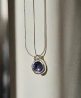 Collar plateado con dije circular con piedra transparente facetada. Cadena fina de eslabones.