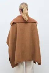 Capa de paño color marrón con cuello solapa y panel central de tejido acanalado. Cuenta con cierre frontal de tres botones grandes y diseño holgado.