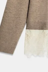 Jersey de punto color beige con cuello redondo y manga larga. Presenta un diseño de bajo combinado con un detalle de encaje en color crema.
