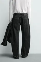Jeans de denim de algodón en color negro con efecto lavado, corte amplio y silueta curva tipo barrel fit con pinzas en las rodillas. Presenta diseño clásico de cinco bolsillos y cierre frontal con cremallera y botón metálico.
