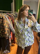 Camisa blanca con estampado de flores azules y verdes, cuello con lazo y mangas largas abullonadas.