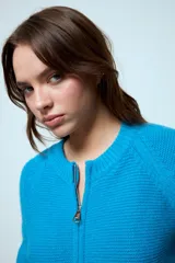 Cardigan corto de punto color rojo, con cierre frontal y cuello redondo. Presenta una textura acanalada y mangas largas.