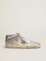 Zapatillas deportivas Golden Goose modelo Mid Star, de caña media, color plateado con detalles en dorado y beige. Presentan una estrella de gamuza en el lateral, perforaciones decorativas y cordones con logo estampado. Suela con efecto desgastado.