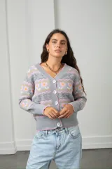 Cárdigan tejido de punto en color beige con diseño de flores y guardas caladas. Presenta escote en V, cierre frontal con botones y terminaciones acanaladas en puños y ruedo.
