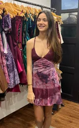 Vestido corto de tela metalizada en tono fucsia con reflejos dorados, con escote en V, diseño de top con triángulos, aberturas laterales en la cintura y doble volado irregular en el ruedo.
