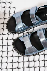 Sandalias chatas con base negra y tiras anchas de cuero sintético color celeste metalizado.