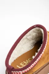 Zueco de gamuza color camel con interior forrado en piel sintética. Presenta una guarda bordada decorativa en el borde superior y una suela de plataforma de goma color marrón.