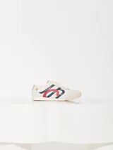 Zapatilla urbana acordonada de cuero vacuno color crema, con detalles en azul y rojo.