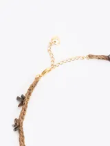 Gargantilla de hilo trenzado color celeste con pequeñas piedras incrustadas a lo largo, cierre de cadena dorada con mosquetón y un dije colgante en forma de corazón marrón con detalles grabados.
