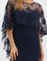 Vestido largo de corte sirena en color azul marino, confeccionado en tejido de punto con caída fluida. Presenta una capa integrada de tul fino sobre los hombros y espalda, decorada con bordados florales a tono y lentejuelas brillantes. Posee escote redondo y cierre invisible en la espalda.
