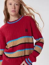 Sweater de punto cable con diseño a rayas horizontales en tonos marrón, amarillo y lila. Presenta cuello redondo acanalado, mangas largas con puños a juego y logo bordado en el pecho.