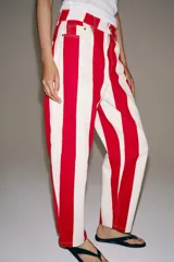 Jeans de tiro medio y corte tapered, con diseño de rayas verticales a contraste en color rojo y blanco. Cuenta con trabillas en la cintura, cinco bolsillos y cierre frontal con cremallera y botón metálico.