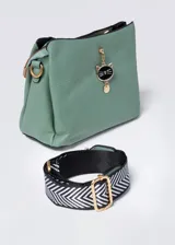 Bandolera verde agua con textura geométrica, cierre superior y correa de tela estampada en blanco y negro. Incluye charm colgante con forma de gato.