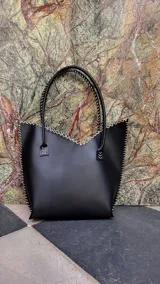 Cartera de cuero mediana con manijas largas, diseño con borde superior en corte en V y terminación artesanal con costuras contrastantes.