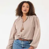 Blusa de corte fluido con estampado de cuadros vichy en tonos beige y blanco. Presenta cuello mao con cordón ajustable terminado en borlas y mangas largas abullonadas con puños elásticos.
