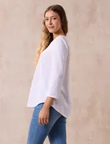 Blusa blanca de tejido labrado con cuello redondo, escote en V y aplique metálico.