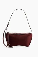 Cartera de hombro color borravino con acabado de textura suave, detalles en material sintético y cierre superior con tirador largo adornado con un nudo decorativo y argollas metálicas. Cuenta con una correa larga ajustable mediante hebilla.