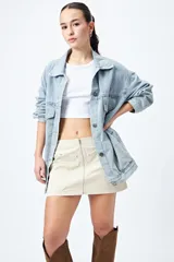 Minifalda color beige de corte recto con cierre metálico frontal visible y bolsillos decorativos con tachas.