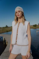 Conjunto de dos piezas tejido en algodón, compuesto por un chaleco sin mangas con cierre frontal de botones y un short de tiro medio. Ambas prendas presentan un diseño en color blanco con detalles de terminaciones en color beige.