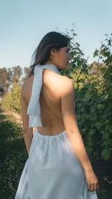 Vestido corto de color blanco con escote halter y espalda descubierta. Presenta un diseño con volado amplio en la parte inferior y caída asimétrica.