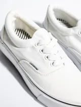 Championes de lona color azul grisáceo, estilo skate o casual, con cordones blancos y suela de goma blanca con una línea fina azul en el borde.