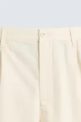 Bermuda de corte regular fit en color beige claro, confeccionada en una mezcla de algodón, lyocell y lino. Presenta pliegues frontales en la cintura, bolsillos laterales y traseros, y cierre frontal con cremallera y botón.