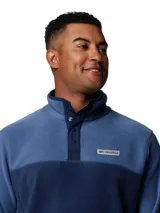 Buzo polar de fleece con diseño de medio cierre frontal con botones a presión. Presenta un diseño bicolor en tonos azul, con cuello alto y logo de la marca bordado en el pecho.