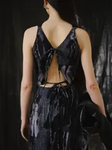 Top sin mangas de escote drapeado y corte relajado a la cintura. Es reversible, con un lado estampado abstracto en tonos negros, grises y azules con efecto glitch, y el otro lado en negro liso.