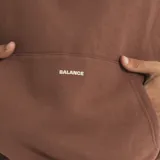 Buzo tipo hoodie color marrón, con capucha, bolsillo frontal tipo canguro y estampado minimalista en el pecho. Presenta un diseño holgado y mangas largas.