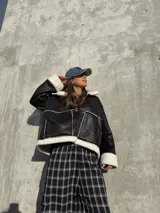 Campera tipo gamulán de cuero sintético negro con interior y detalles de corderito blanco. Presenta cierre frontal, bolsillos laterales y diseño holgado.