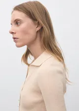 Jersey de punto fino color beige, con cuello camisero, manga corta y cierre frontal con botones pequeños. Diseño entallado de canalé.