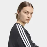 Buzo Adidas de cuello redondo con corte oversize, confeccionado en tejido de punto. Presenta las icónicas tres franjas blancas en las mangas y el logo del trifolio bordado en el pecho.