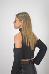 Blusa corta negra con cuello alto, hombros descubiertos y mangas largas.