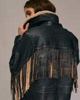 Chaqueta de cuero negra con cuello de borrego color crema, cierre de botones y flecos de cuero en las mangas.