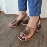 Sandalias de cuero color bronce, con taco cuadrado y tira ajustable con hebilla en el talón.