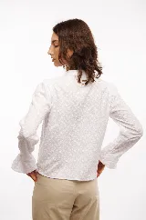 Camisa blanca de algodón bordado con motivos florales, cuello mao, botones al frente y terminación con bordes redondeados.