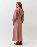 Vestido camisero largo de algodón con estampado a cuadros en tonos rojo y blanco, cuello clásico, mangas largas abullonadas y cinturón ajustable del mismo género.