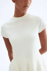 Top de punto fino color blanco, con cuello redondo acanalado, mangas cortas raglán y silueta acampanada tipo peplum en el bajo.