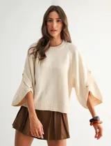 Buzo de punto beige con mangas tres cuartos anchas, cuello redondo y detalle de botones en las mangas.