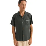 Camisa verde oscuro de manga corta con cuello cubano, cierre con botones y bolsillo en el pecho con ribete blanco.