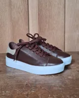 Zapatilla urbana de cuero con diseño combinado en color dorado metalizado y gamuza en tono tostado. Presenta cordones al tono, suela de goma blanca y detalles en cuero marrón en la parte posterior.