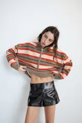 Jersey de punto con diseño de rayas horizontales en tonos gris, rojo y crema. Presenta cuello perkins, cierre frontal con cremallera metálica y mangas largas con hombros caídos.