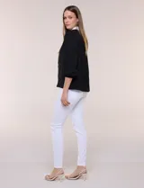 Blusa negra de calce suelto y caída ligera con sutil textura, cuello camisero blanco, escote en V con pechera en contraste y mangas tres cuartos abullonadas con puños elásticos.