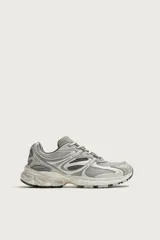 Zapatilla deportiva estilo running color gris, con diseño técnico en capas, suela gruesa con volumen y detalles reflectantes.