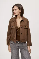 Campera negra de efecto gamuzado con cuello camisero, cierre frontal de botones, bolsillos plaqué en el pecho y detalles de costuras decorativas y calados.